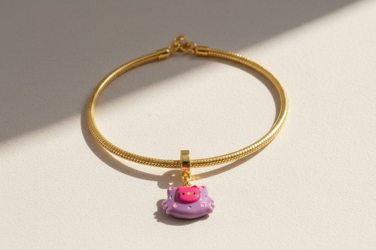 Gold bracelet with a pink cat charm on a wrist against a neutral background