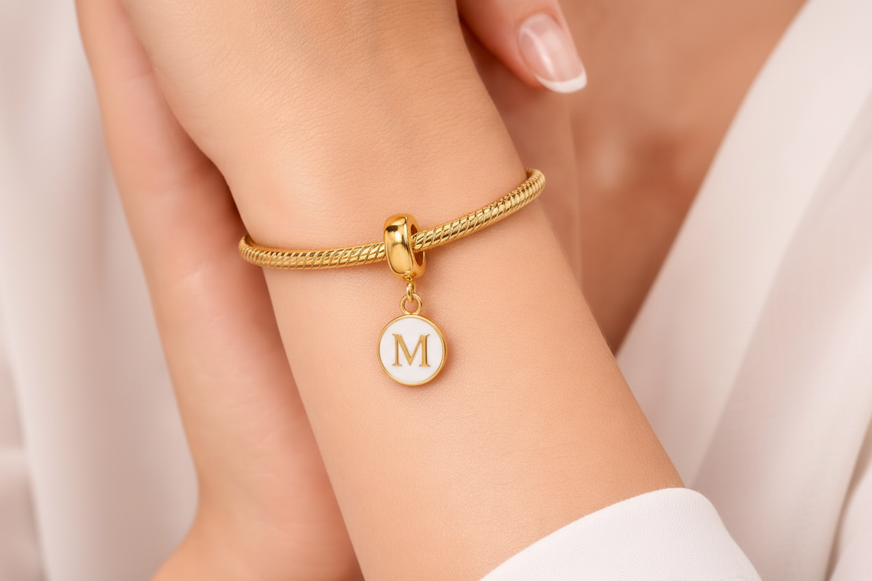 Gold bracelet with a round charm on a person's wrist against a neutral background
