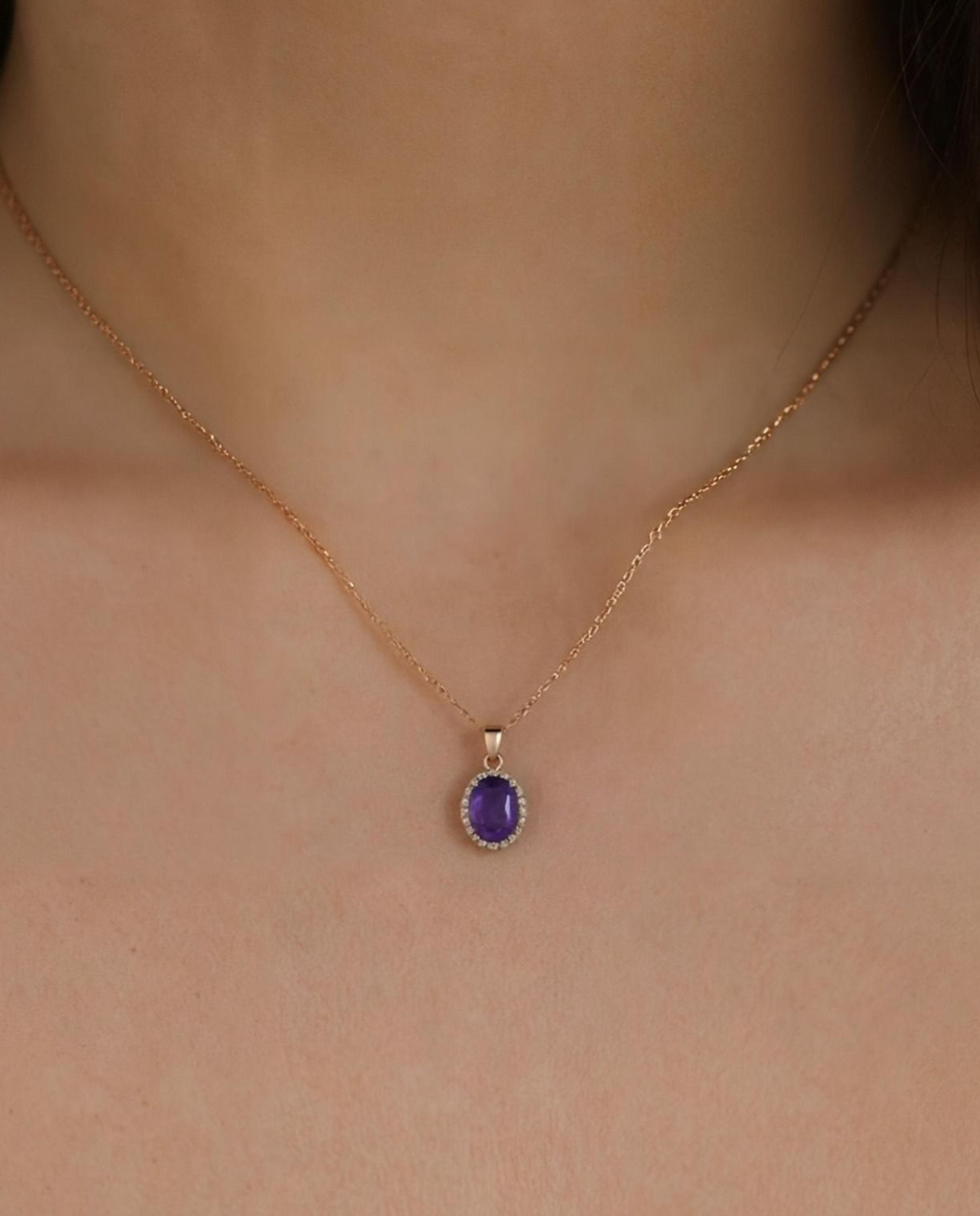Gold necklace with a purple gemstone pendant on a person's neck