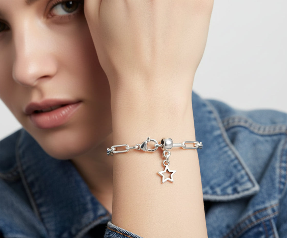 Close-up of a person wearing a silver bracelet with a star charm, against a neutral background.