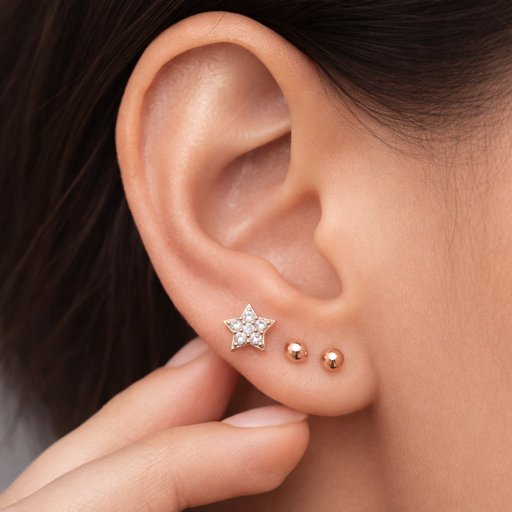 Close-up of an ear wearing a set of rose gold ball and star-shaped earrings