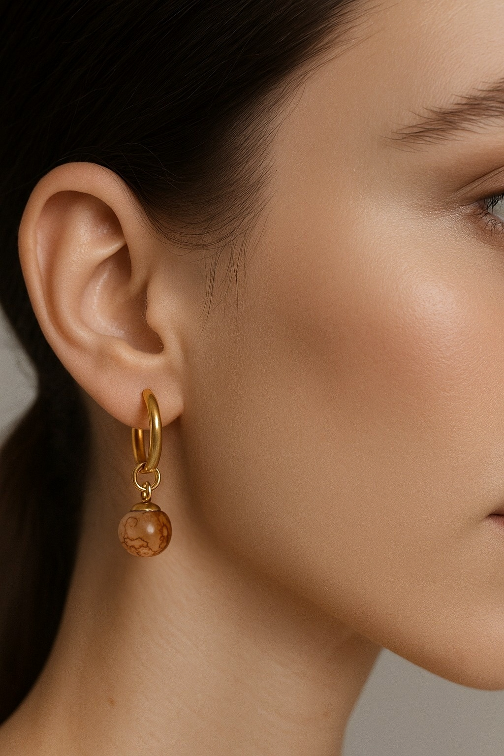 Close-up of a gold hoop earring brown glass bead dangle charms
