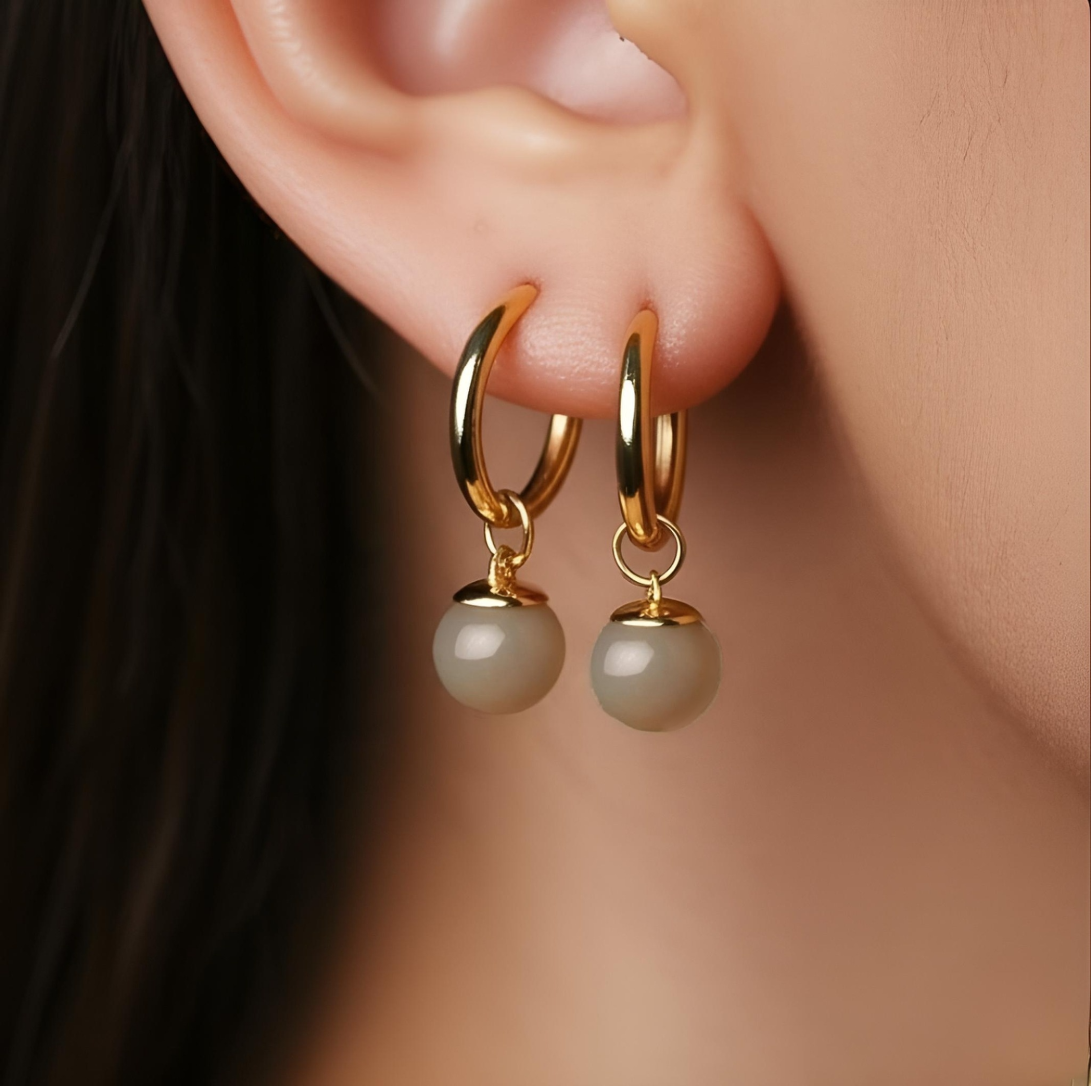 Gold hoop earrings with grey gemstones drops worn by a person.