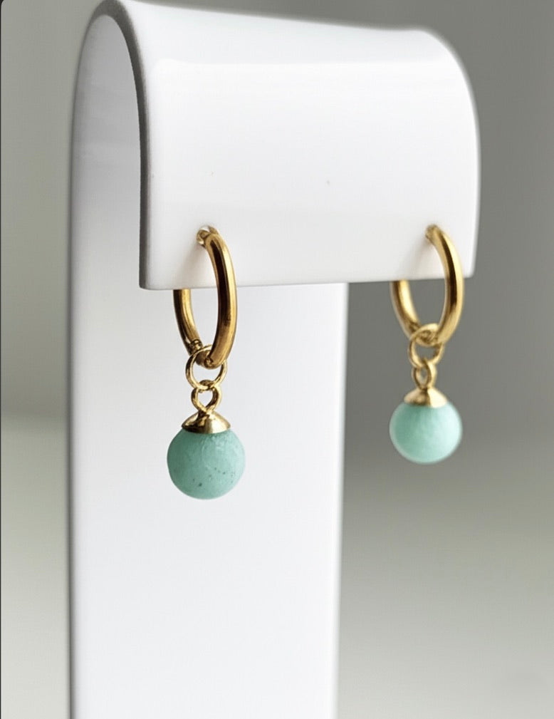 Gold hoop earrings with green beads on a white stand.