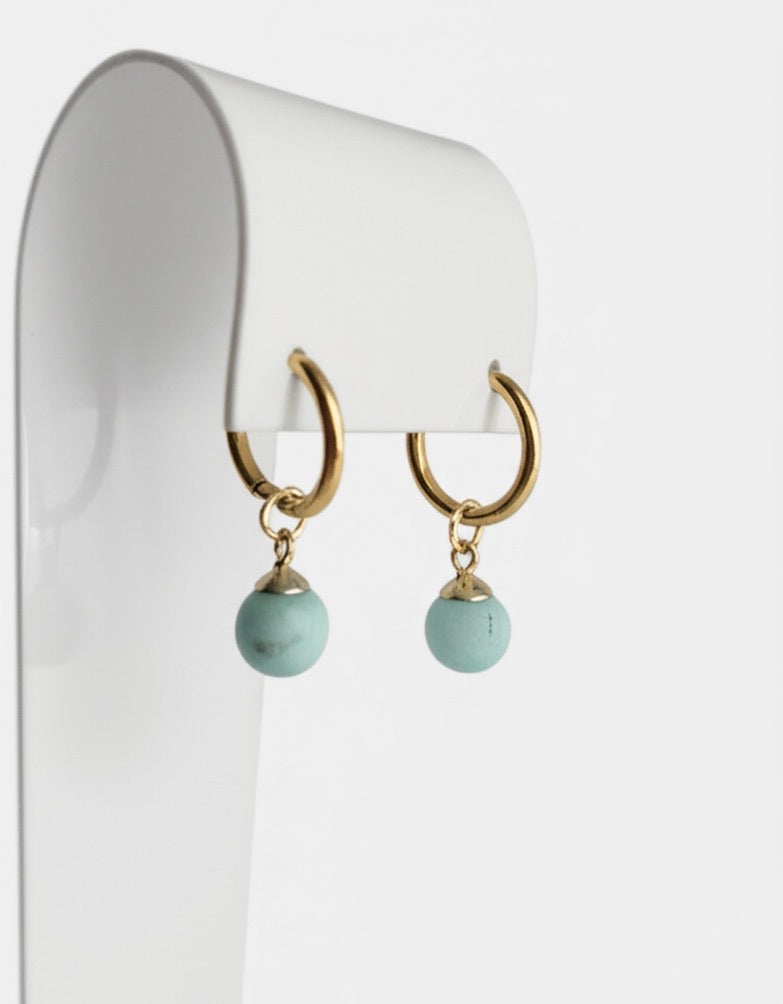 Gold hoop earrings with natural gemstone beads on a white stand