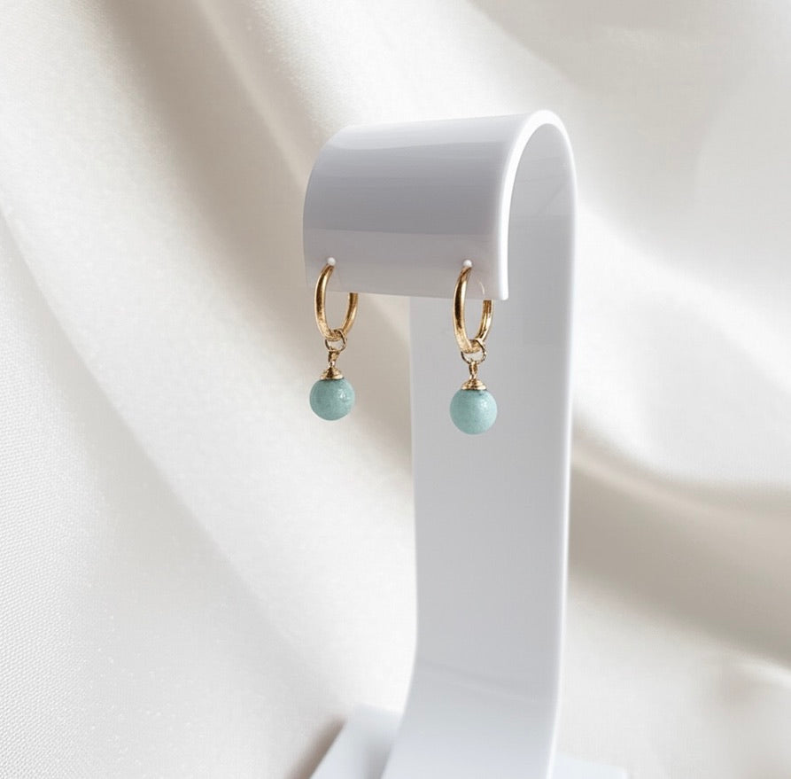 Gold hoop earrings with green natural gemstone beads on a white stand
