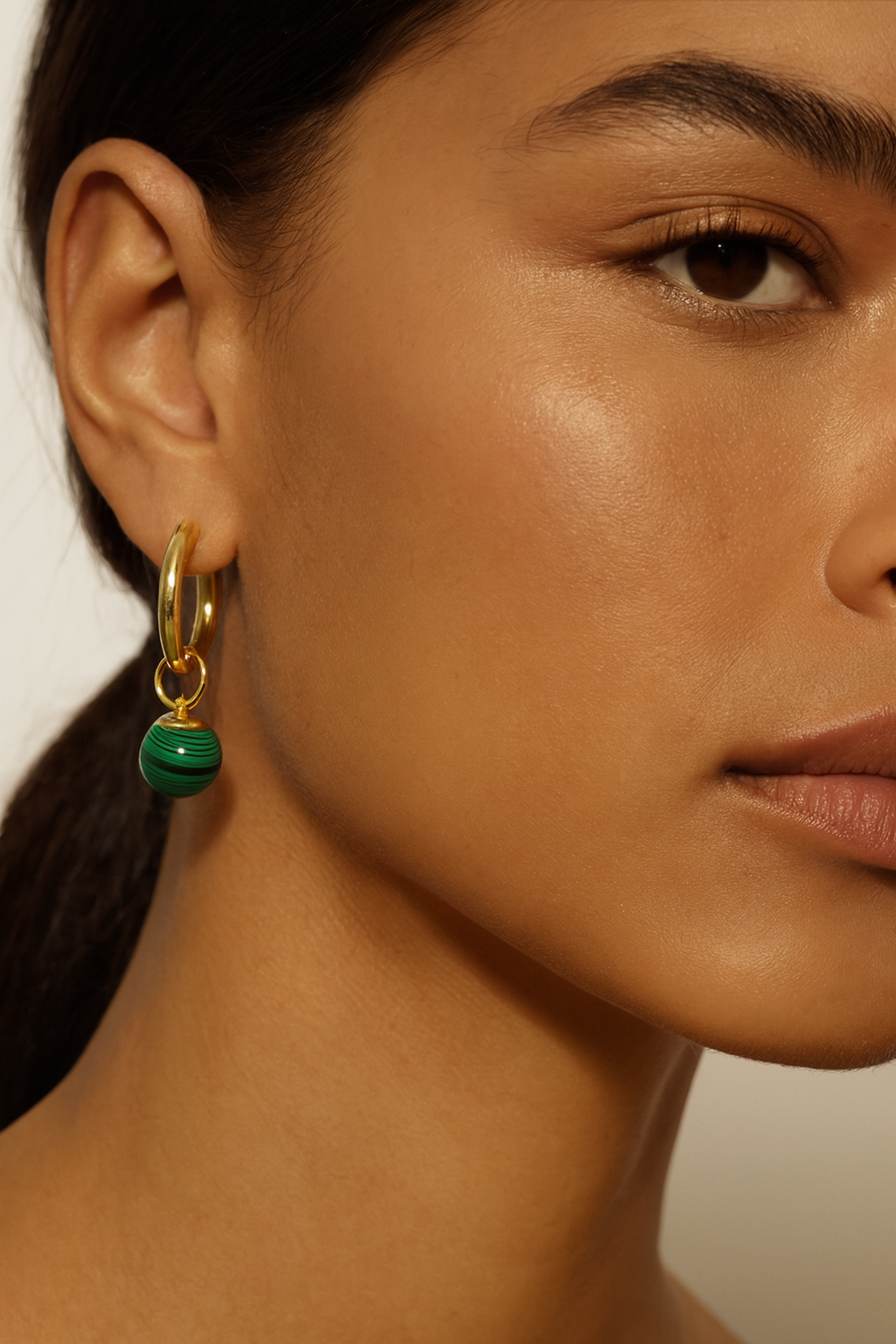 Close-up of a person wearing a gold earring with a green dangle charms.