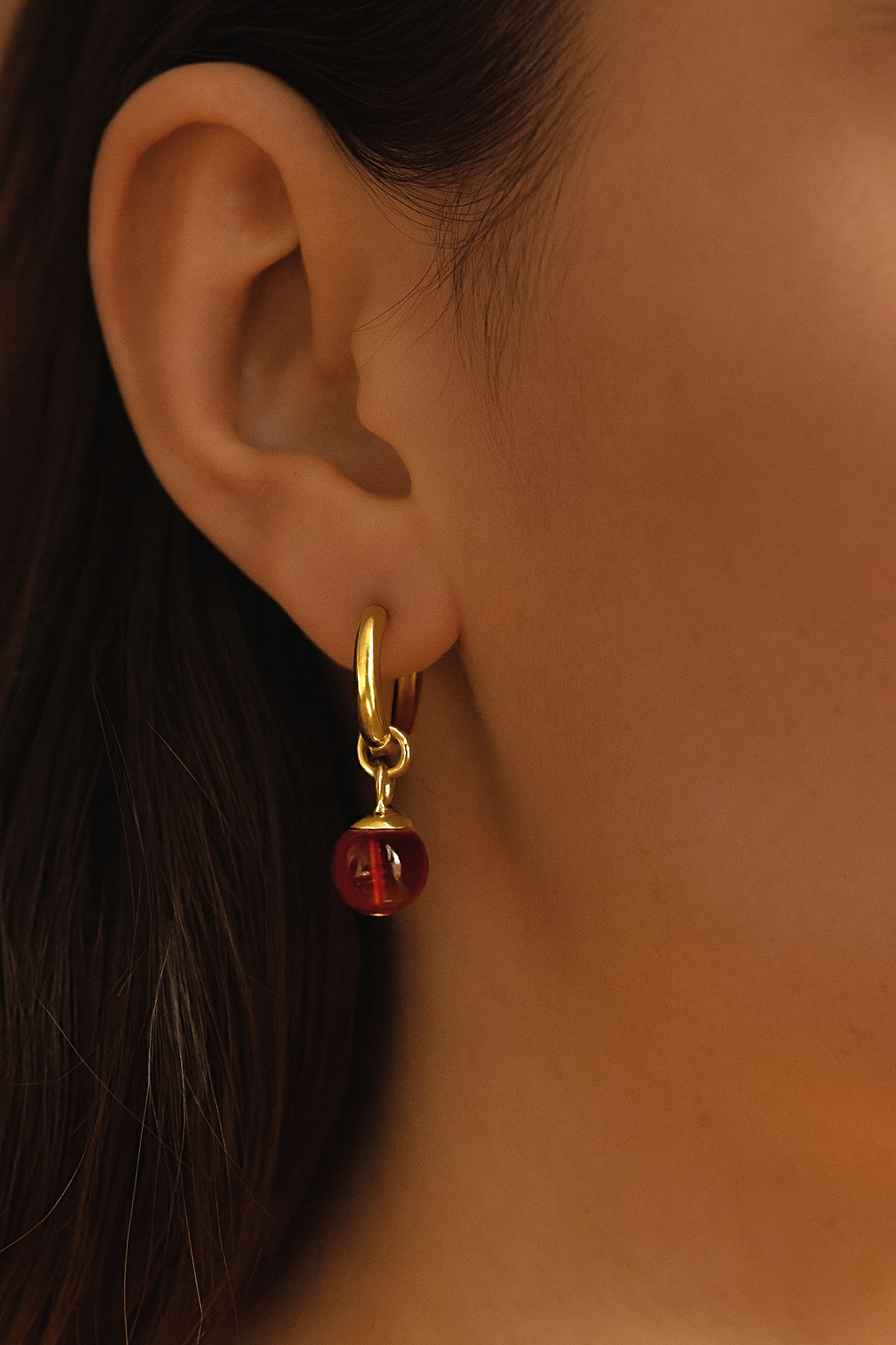Gold hoop earring with a red gemstone worn by a person.