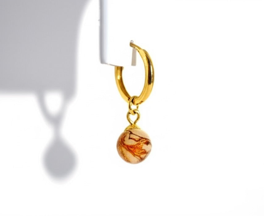 Gold hoop earring with a small round glass charm on a white background