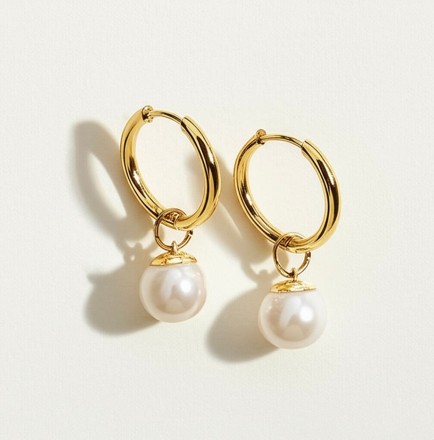 Gold hoop earrings with seashell pearl charms on a light background