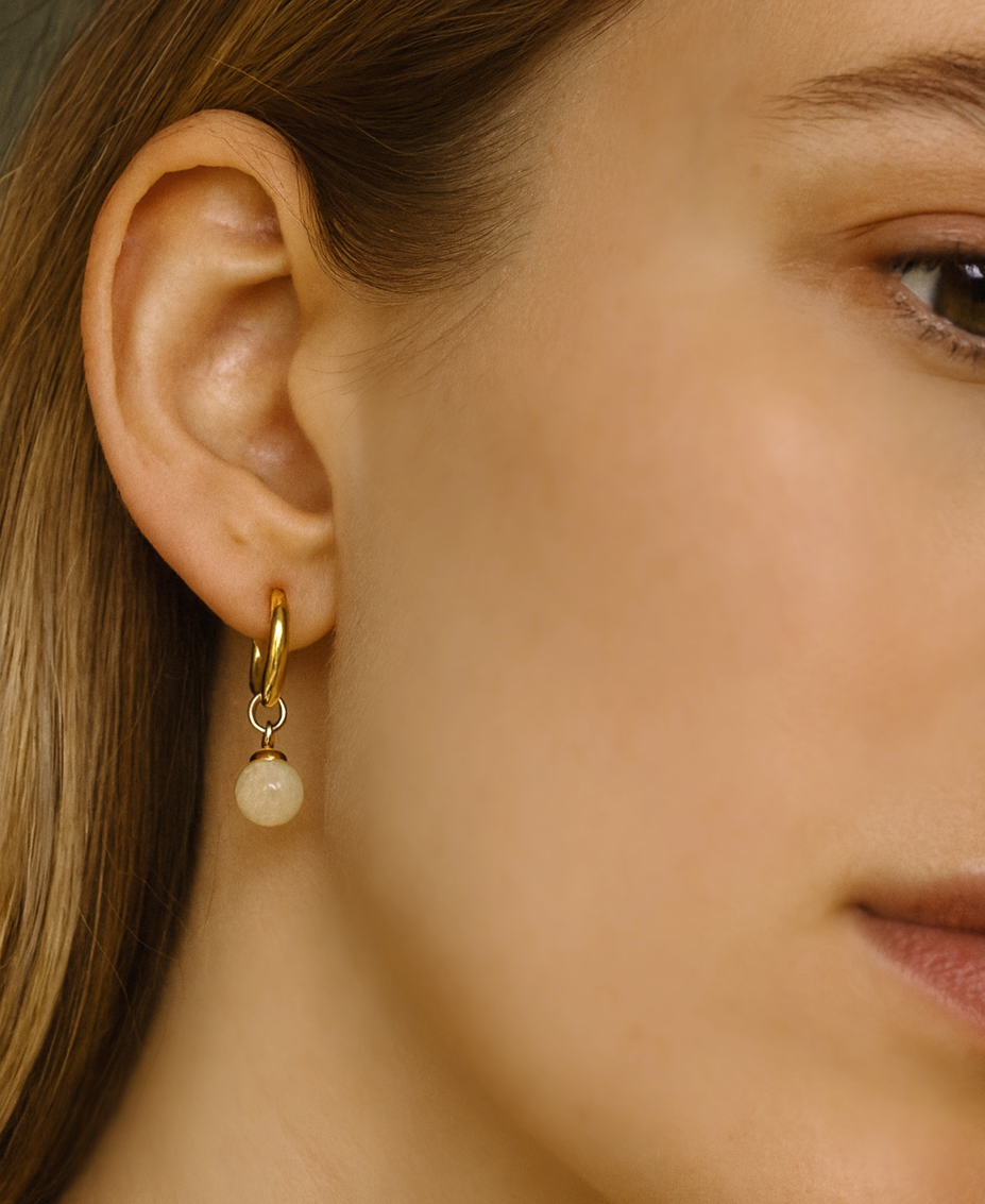 Close-up of a person wearing a gold earring with a yellow gemstone bead drop.