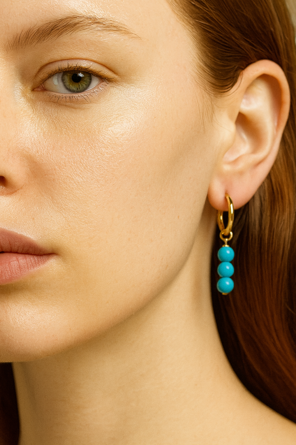 Close-up of a person wearing turquoise dangles on earrings with gold hooks.
