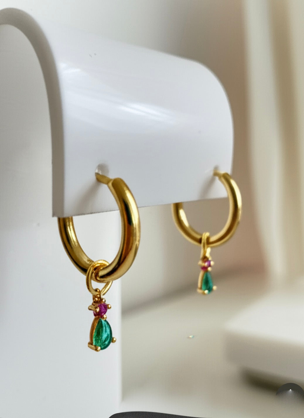 Gold hoop earrings with cubic zirconia drops charms on a white stand.