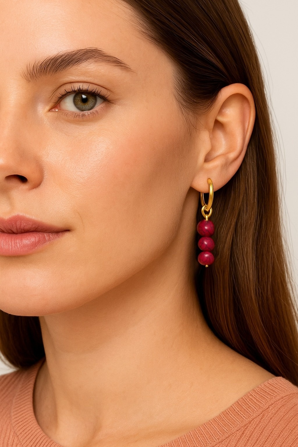 Close-up of a woman wearing a gold hoops earring with attached red beads charms