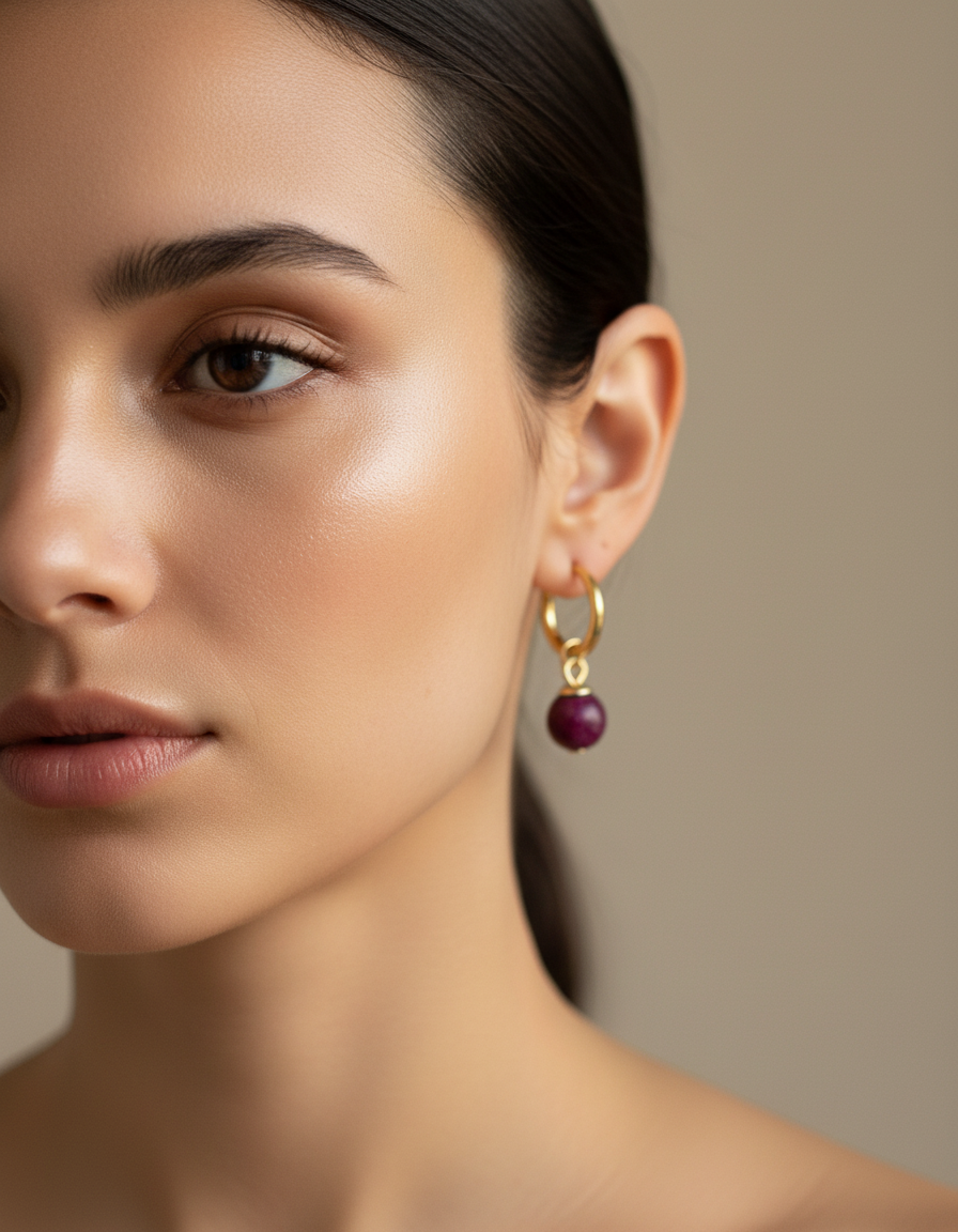 Close-up of a woman wearing a gold earring with a red garnet gemstone beads against a neutral background