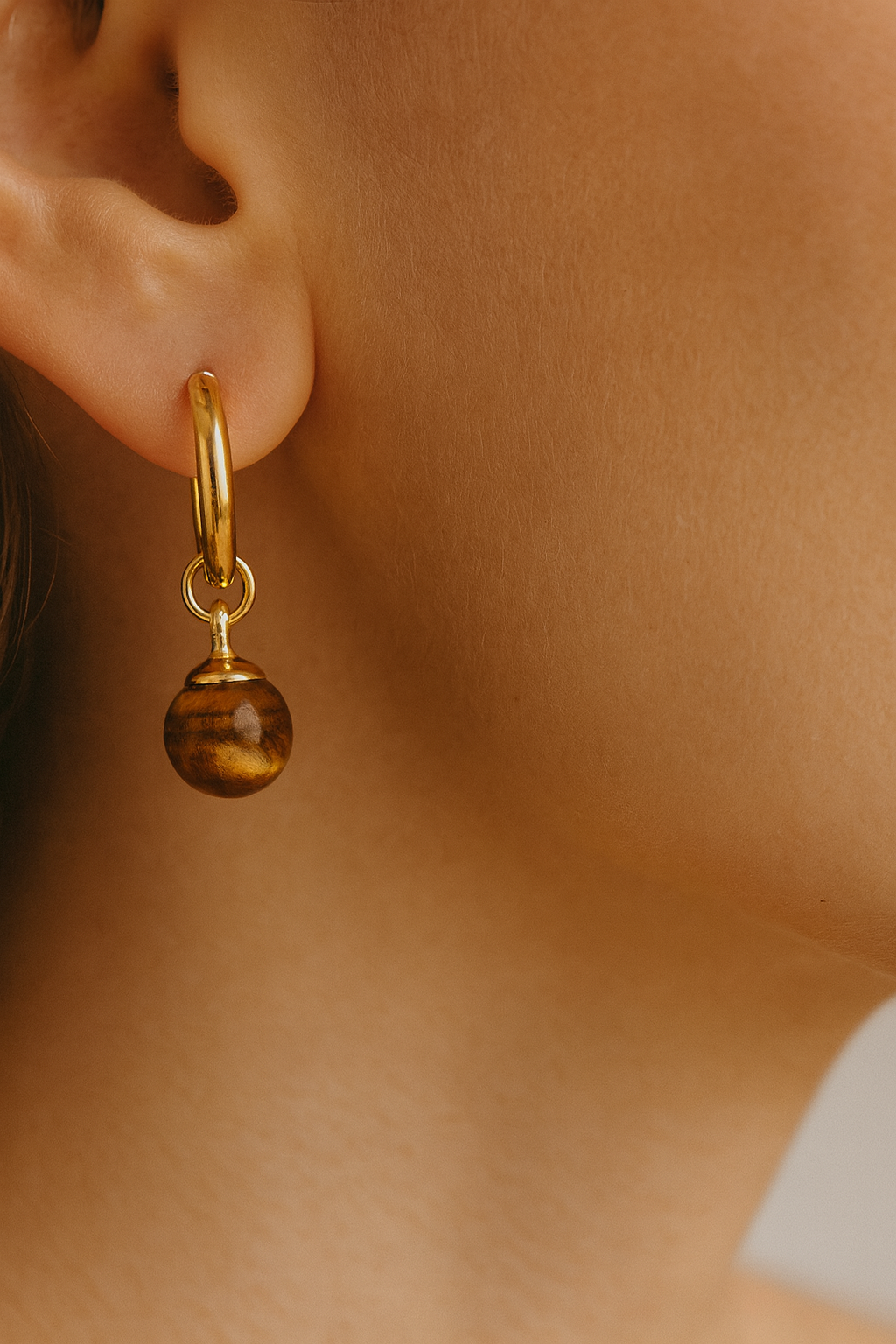 Gold earring with a tiger eye gemstone charms worn by a person.