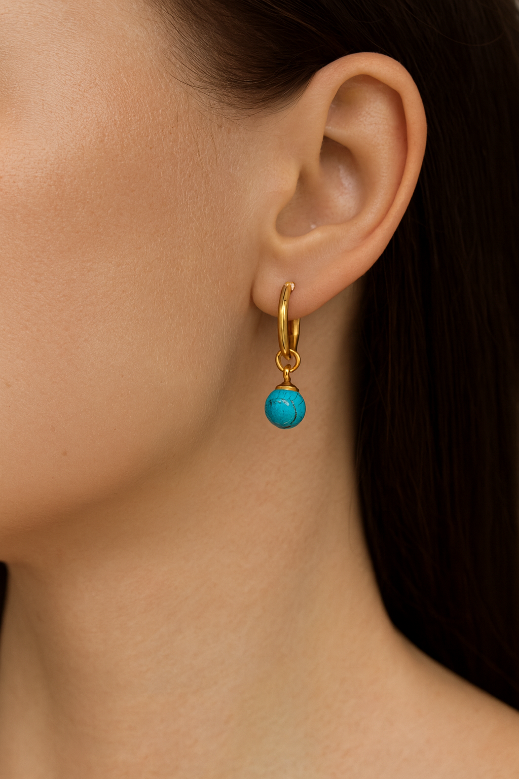 Gold earring with a turquoise bead worn by a person