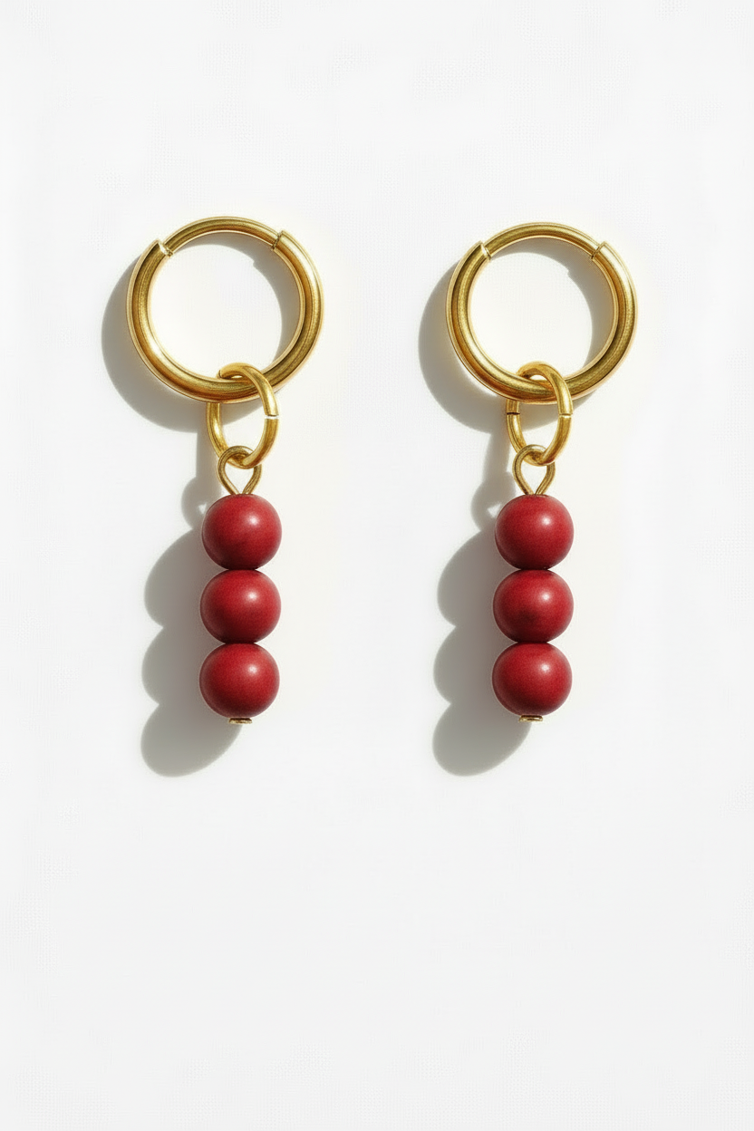 Gold hoop earrings with red beads on a white background