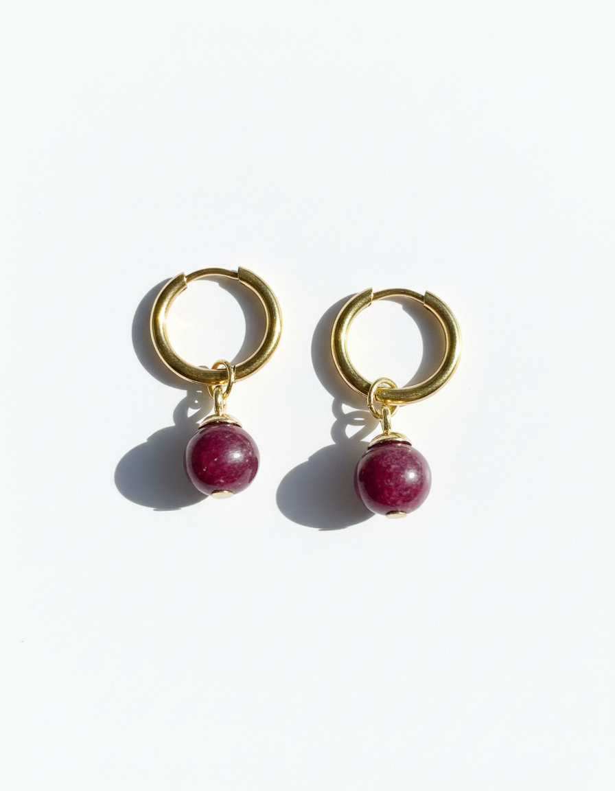 Gold hoop earrings with dark red gemstone beads on a white background