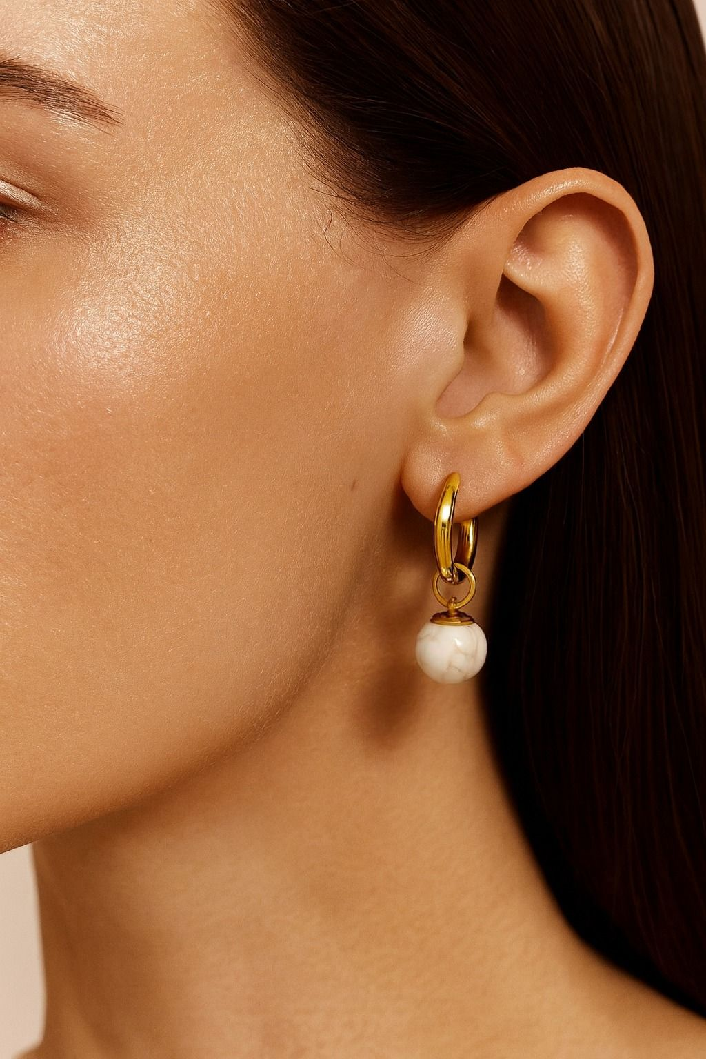 Close-up of a gold earring with a white gemstone drop on a person's ear.