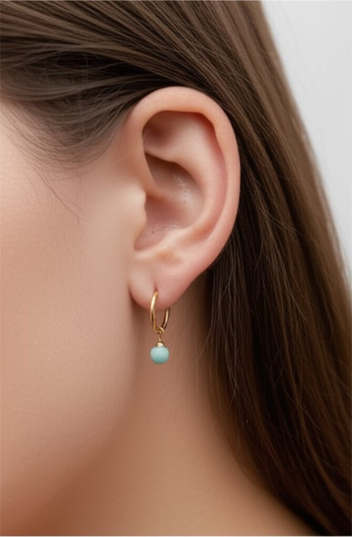 Close-up of an ear wearing a gold hoop earring with a turquoise bead.