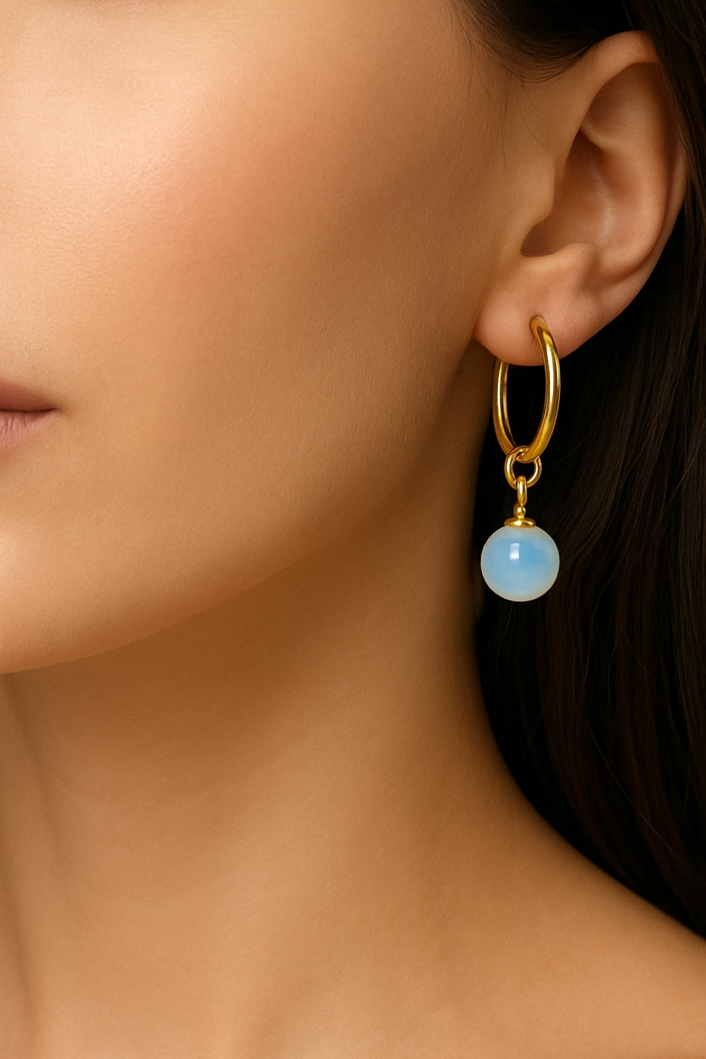 Close-up of a gold hoop earring with a blue gemstone worn by a person.