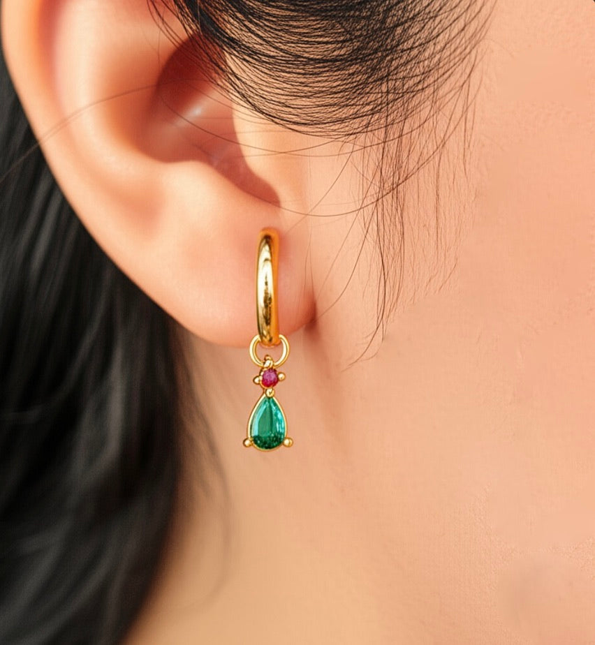 Gold hoop earring with a green teardrop and red gemstone worn by a person.