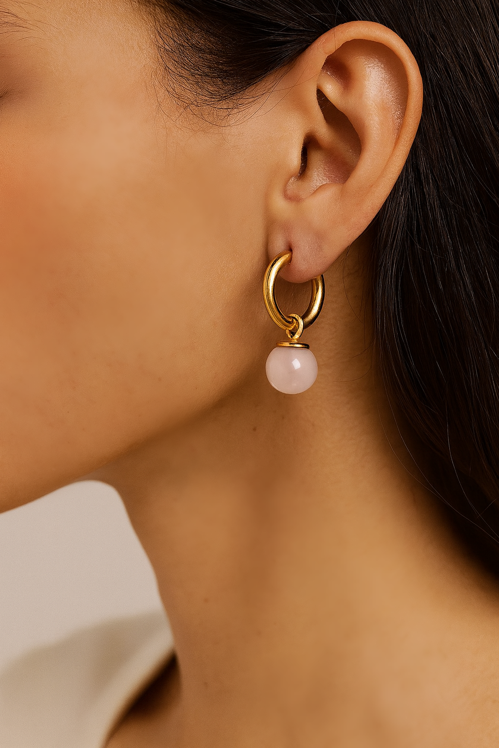 Close-up of a gold earring with a pink gemstone dangles worn by a person.